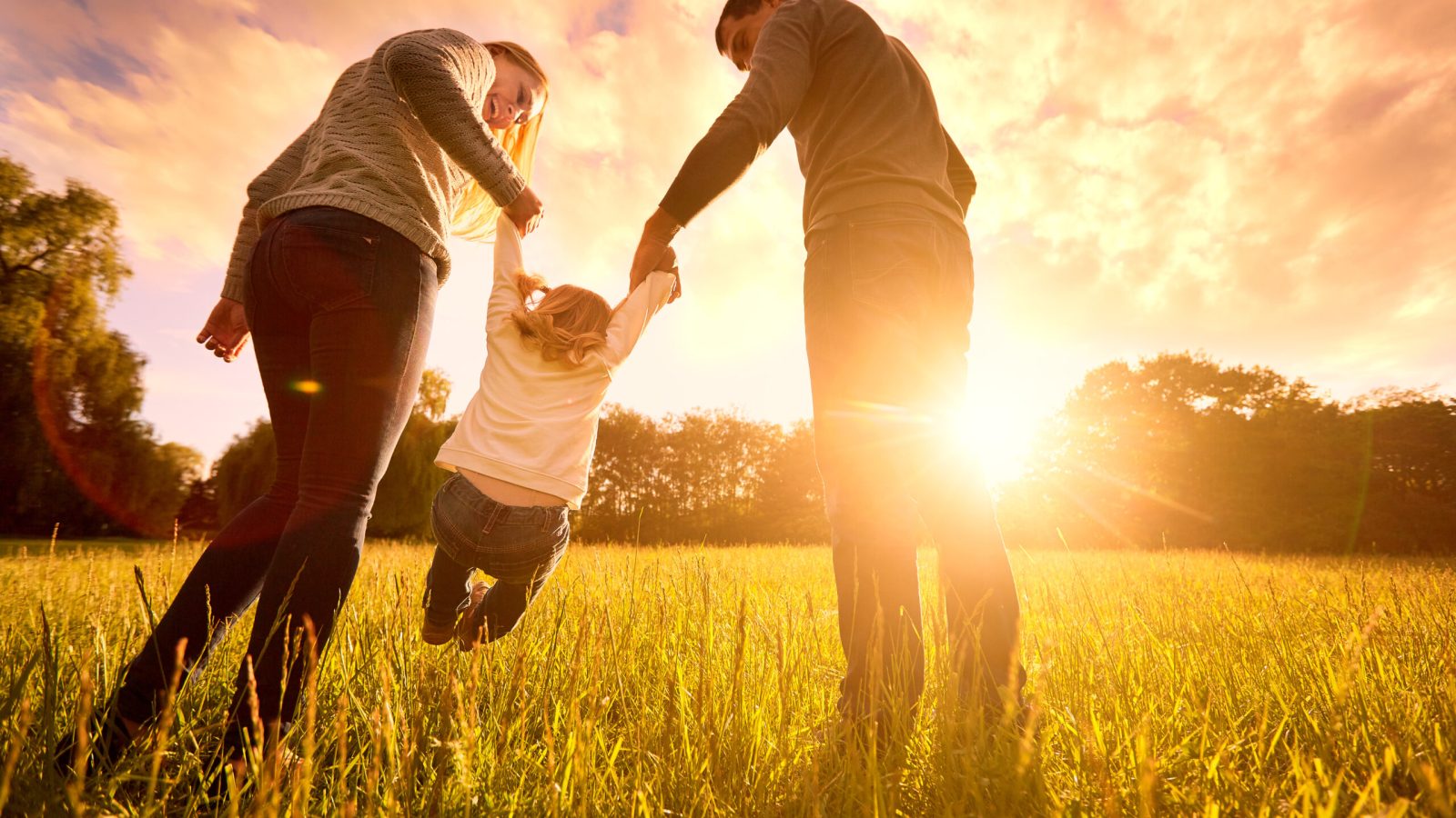 Happy family in the park evening light. The lights of a sun. Mom, dad and baby happy walk at sunset. The concept of a happy family.Parents hold the baby's hands.