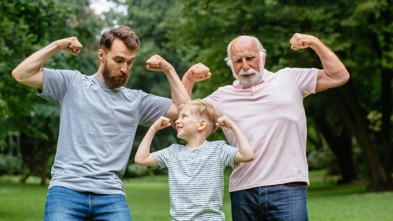 Portrait og happy family - grandpa, father and his son smiling and showing their muscles outdoor in park on background. Three different generation concept.