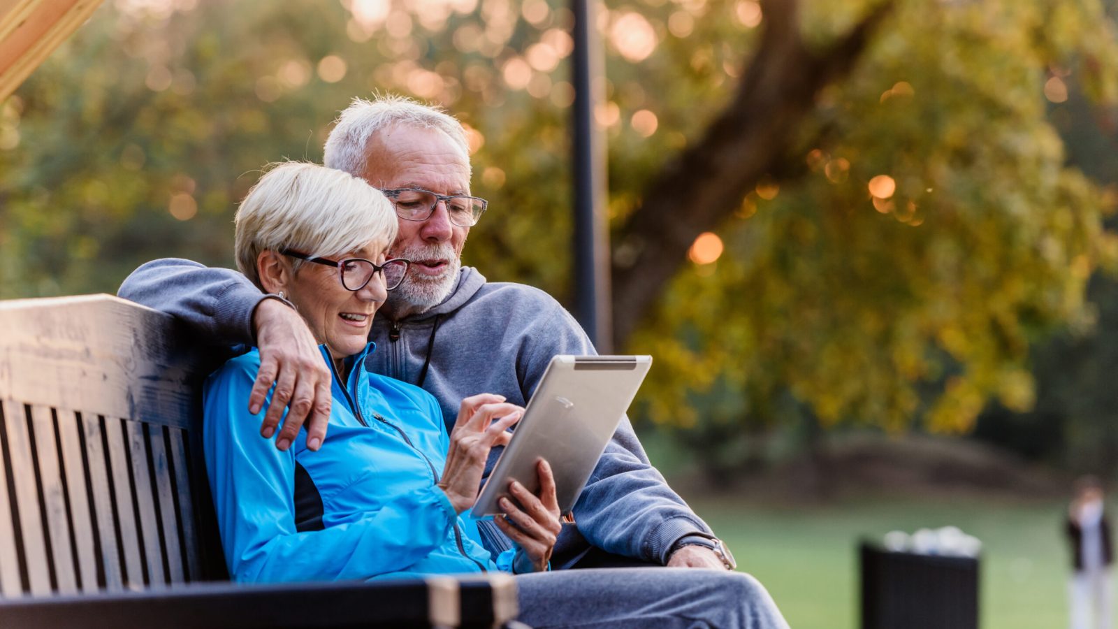 Smiling senior active couple sitting on the bench looking at tab