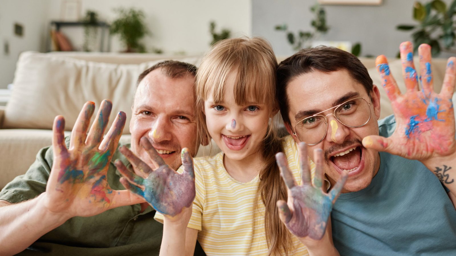 Portrait of happy gay family with child showing their painted hands and smiling at camera